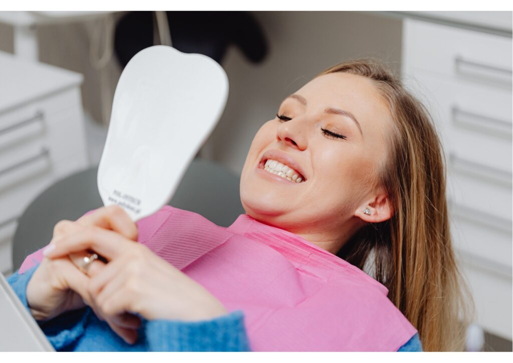 Patient smiling and holding a mirror after cosmetic dental treatment in a dental chair.