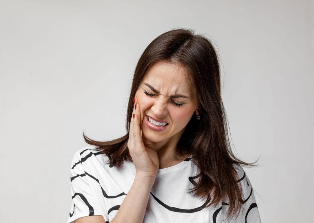 Woman holding her jaw in discomfort, illustrating common symptoms of teeth grinding and the need for treatment to fix grinded teeth and restore damaged enamel.