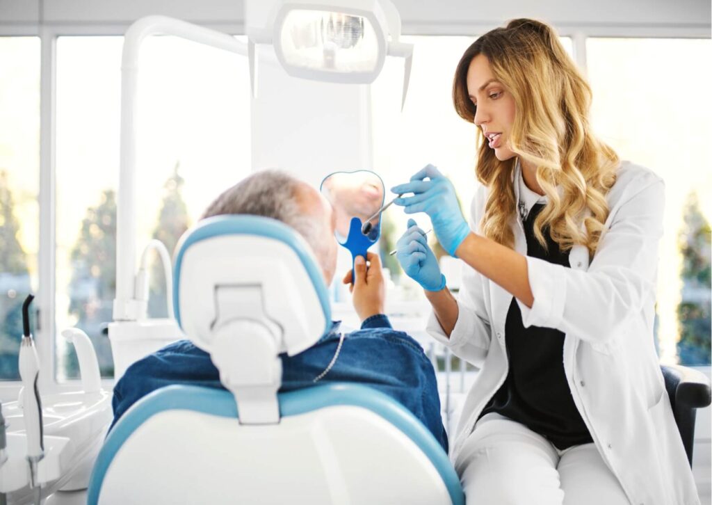 Dentist using a mirror to explain areas of tooth decay to a patient during a routine dental examination.